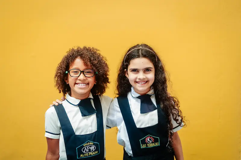 Dos niñas sonrientes con uniforme escolar del Preescolar Las Terrazas en Caracas posando frente a un fondo amarillo.