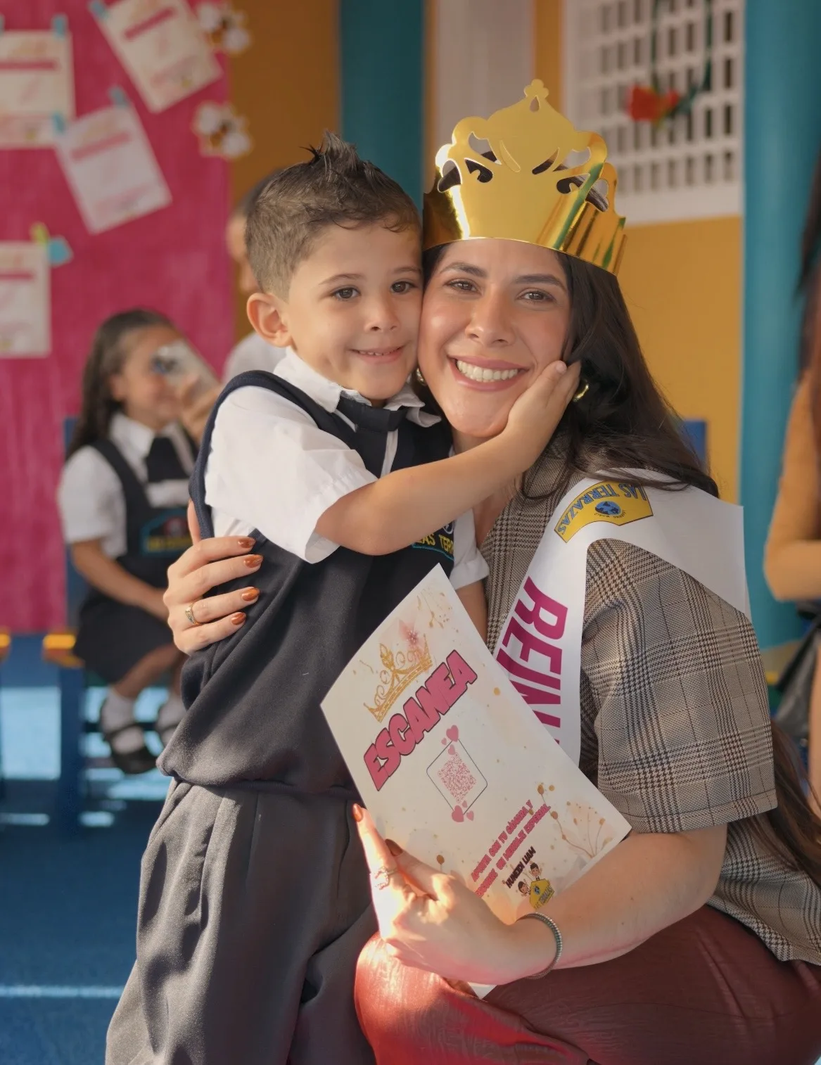 Madre con corona y niño con uniforme escolar en evento del Preescolar Las Terrazas